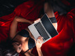 © Vitte Yevhen - Close up of Sexy young brunette woman in black sensual lingerie and in stockings using laptop on red bed in studio.