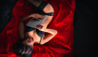 © Vitte Yevhen - Sexy young brunette woman in black sensual lingerie and in stockings using laptop on red bed in studio.