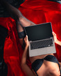 © Vitte Yevhen - Close up of Sexy young brunette woman in black sensual lingerie and in stockings using laptop on red bed in studio.