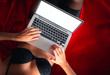 © Vitte Yevhen - Close up of Sexy young brunette woman in black sensual lingerie and in stockings using laptop on red bed in studio.