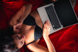 © Vitte Yevhen - Close up of Sexy young brunette woman in black sensual lingerie and in stockings using laptop on red bed in studio.