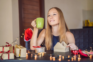 Young woman is packing presents. Present wrapped in craft paper with a red and gold ribbon for christmas or new year. Woman makes an advent calendar for her child