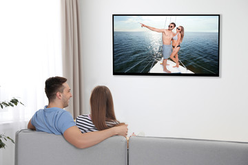 Poster - Young couple watching TV on sofa at home