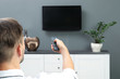 Man switching channels on plasma TV with remote control at home