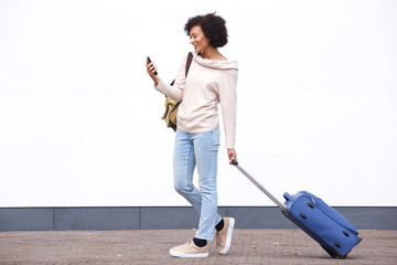 Wall Mural - Full body smiling african american travel woman walking with mobile phone  and suitcase boy white wall