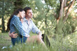 © soleg - young couple sitting on the grass in the forest and looking on sunset, summer nature, bright sunlight, shadows and green leaves, romantic feelings
