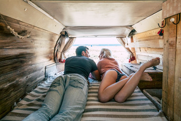 Beautiful young millennial couple people lay down together inside a little cozy van enjoying vanlife and alternativer hipster vacation parked at the beach - happiness and travel concept for youth