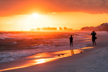 Young Couple Looking At Dramatic Orange Red Sunset In Santa Rosa Beach, Florida With Pensacola Coastline Coast Skyline In Panhandle With Ocean Gulf Mexico Waves