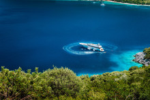 Luxury White Yacht Sail Boat Anchoring In A Tranquil Bay In Deep Blue Water Water, Near Picturesque Shore Of Greek Islands