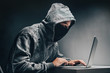 © wpadington - Cyber crime. Male hooded hacker with hidden face accessing to personal information on a computer in the dark. Technologal, cyber crime concept