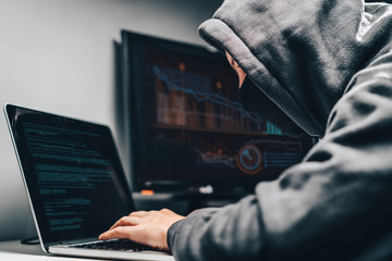 cyber crime. male hooded hacker with hidden face accessing to personal information on a computer in 