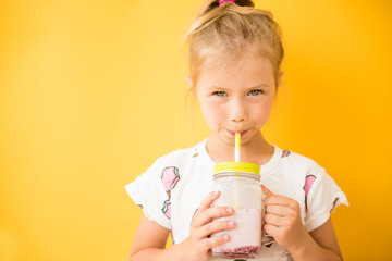 Little girl standing with milkshake in hand on yellow background