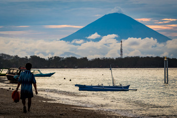 Wall Mural - Local fisherman walking along the beach with a volcano and boats in the background