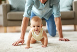 Fototapeta  - family, fatherhood and parenthood concept - happy little baby girl with father at home crawling on floor