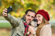Frau und Mann mit Hund beim Herbst Spaziergang nehmen ein Selfie mit dem Handy auf, Hund schleckt ins Gesicht