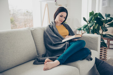 Portrait of nice lovely sweet tender attractive charming calm peaceful straight-haired girl sitting barefoot on divan reading poems stories in light interior room