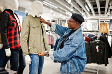 Stylish Casual African American Man At Jeans Jacket And Black Beret At Clothes Store Looking On New Jacket On Mannequin.