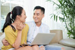 © DragonImages - Beautiful casual ethnic couple sitting on couch with laptop spending time at home in leisure