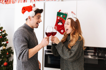 Canvas Print - Photo of young couple man and woman 20s clinking glasses with wine, while celebrating New Year in apartment