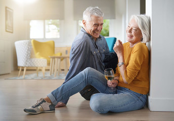 Relaxed senior couple sitting on floor in modern home with glass of wine