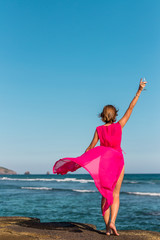 Wall Mural - Young woman in a long red dress and with a glass of wine posing on the sea background.