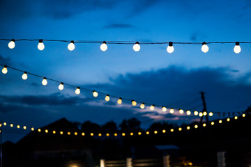 row of hanging summer terrace lights during evening, small outdoor light bulbs.