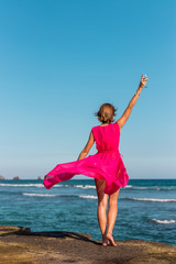 Wall Mural - Young woman in a long red dress and with a glass of wine posing on the sea background.