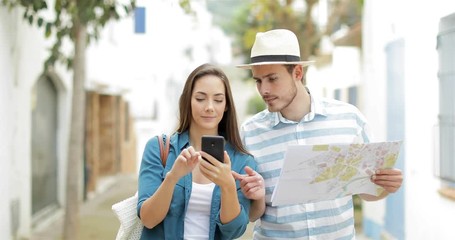 Wall Mural - Couple of excited tourists walking in the street finding best online offer on a smart phone on vacation