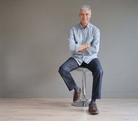  Full length casual senior man sitting on stool on gray background