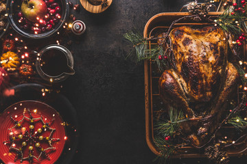 Christmas dinner table with whole roasted turkey, stuffed with dried fruits served with sauce,red plates, cutlery, decoration and burning candles,  top view. Traditional Christmas food. Copy space