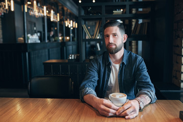 Confident man enjoying a cup of coffee while having work break lunch in indoors cafe looking pensive