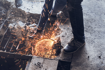 Male worker saws a disk grinding saw armature into a reinforced concrete panel, the destruction of the old house. Sparks from friction with metal. Rescue work.