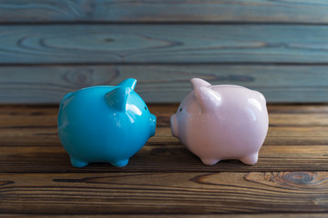 Two piggy banks, pink and blue, stand nose to nose, guinea pigs. On the wooden background. Concept business ideas, economics, savings, banking, symbol of the new year.