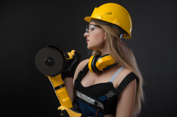 Female construction worker in a hard hat with angle grinder over black background