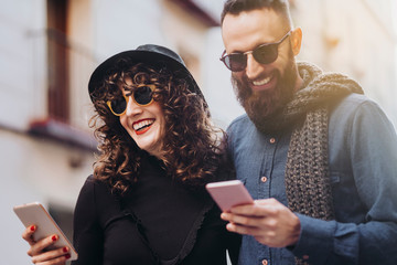 Two happy friends using the mobile in the street. Friendship concept.