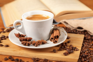 Wall Mural - Coffee break a Cup of hot coffee and a book on a wooden table. A white Cup of black coffee surrounded by a small amount of roasted coffee beans, cinnamon, anise and an open book