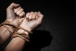 © adragan - Man with hands tied with rope on black background. The concept of slavery or prisoner. Copy space for text.