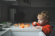 © Cavan Images - Blond girl eating orange by countertop in kitchen