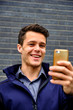 © Cavan Images - Smiling young businessman video conferencing using smart phone against wall in city