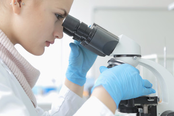 Young female male scientist looking through a microscope in a laboratory doing research, microbiological analysis, medicine.