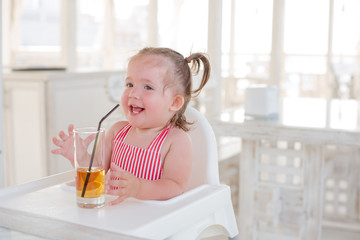 A little smiling toddler girl is sitting at a table in a summer cafe in the seaside resort.