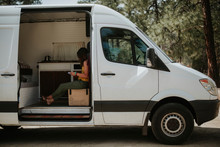 Side View Of Woman Reading Book While Sitting In Motor Home At Forest