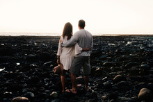 Rear View Of Couple Looking At Sea While Standing On Rocks Against Clear Sky