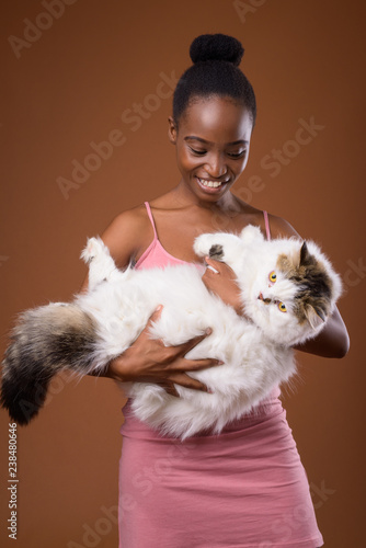 Fényképezés Young beautiful African Zulu woman holding cat while smiling