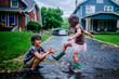 © Cavan Images - Side view of playful sister splashing puddle on brother during rainy season