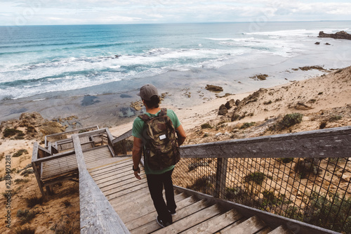 Fotomural Rear view of hiker with backpack walking down wooden steps at beach