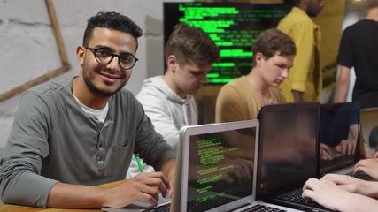 Portrait of friendly young Asian man in glasses looking at camera and smiling during programming workshop
