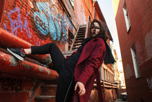 Low Angle Portrait Of Confident Woman Wearing Red Coat While Climbing On Building In City
