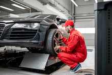 Car Service Worker In Red Uniform Changing Wheel Of A Sport Car At The Tire Mounting Service
