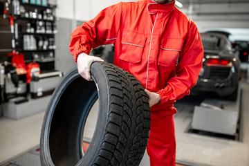 Wall Mural - Worker in uniform carrying new tires at the car service or store, close-up view